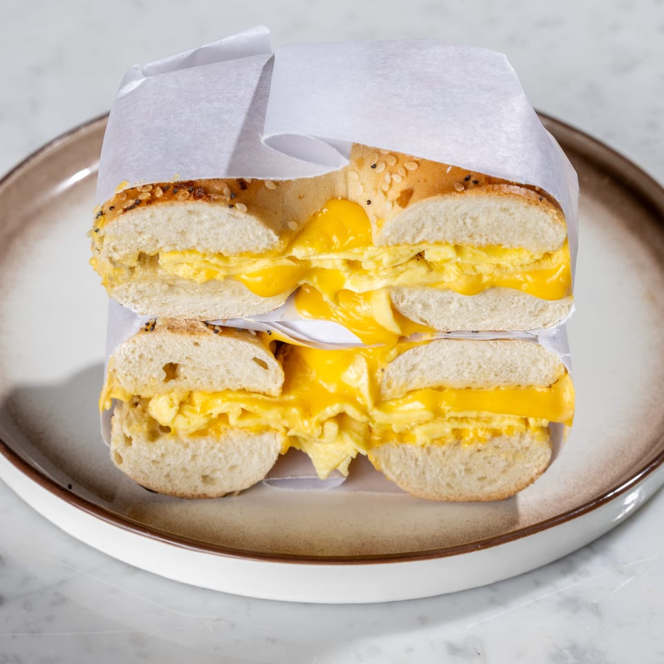 Everything bagel sandwich, cut in half, filled with scrambled eggs and melted cheese on a plate.
