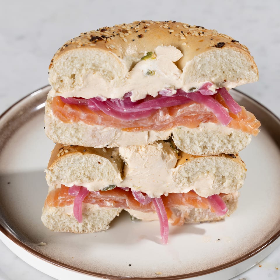 Everything bagel with cream cheese, smoked salmon, and pickled red onions, stacked on a plate.